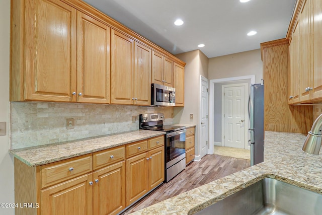 kitchen with sink, light wood-type flooring, appliances with stainless steel finishes, light stone countertops, and decorative backsplash