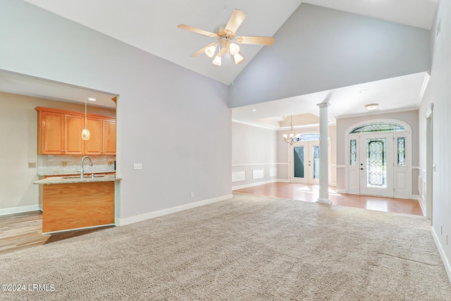 unfurnished living room featuring decorative columns, ceiling fan with notable chandelier, light colored carpet, and high vaulted ceiling