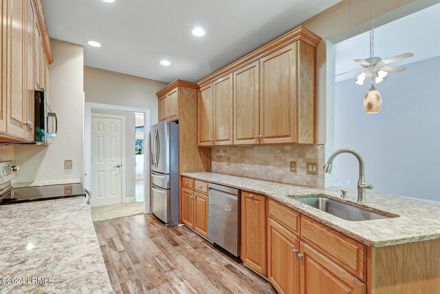 kitchen with sink, light stone counters, tasteful backsplash, light wood-type flooring, and appliances with stainless steel finishes