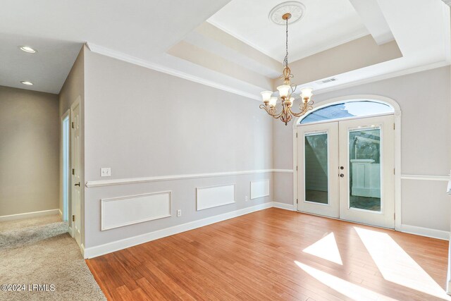 unfurnished room with french doors, a chandelier, ornamental molding, a tray ceiling, and hardwood / wood-style floors