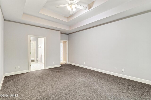 unfurnished bedroom with carpet floors, a tray ceiling, ensuite bath, and ceiling fan