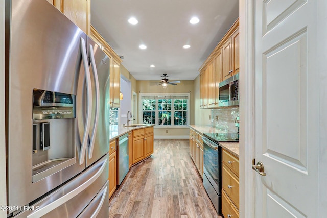 kitchen featuring appliances with stainless steel finishes, sink, ceiling fan, light stone countertops, and light hardwood / wood-style flooring