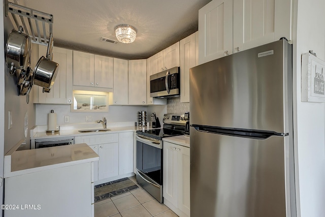 kitchen with sink, a textured ceiling, light tile patterned floors, appliances with stainless steel finishes, and white cabinets