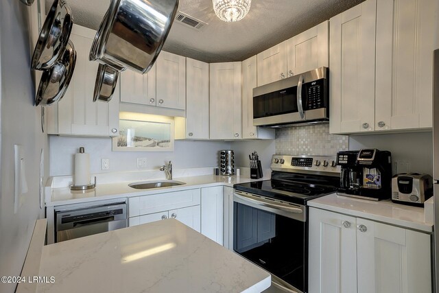 kitchen with sink, light stone counters, a textured ceiling, stainless steel appliances, and white cabinets