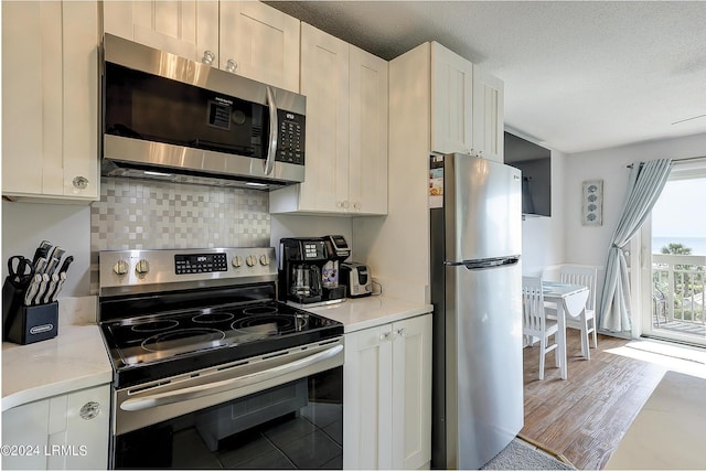 kitchen with white cabinetry, stainless steel appliances, light hardwood / wood-style floors, a textured ceiling, and decorative backsplash