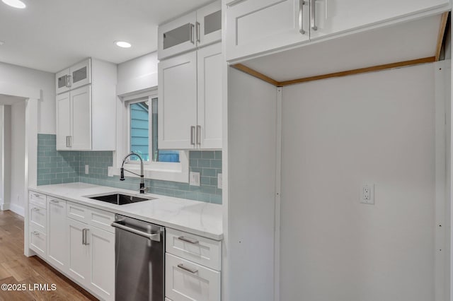 kitchen with backsplash, dishwasher, light stone countertops, and a sink