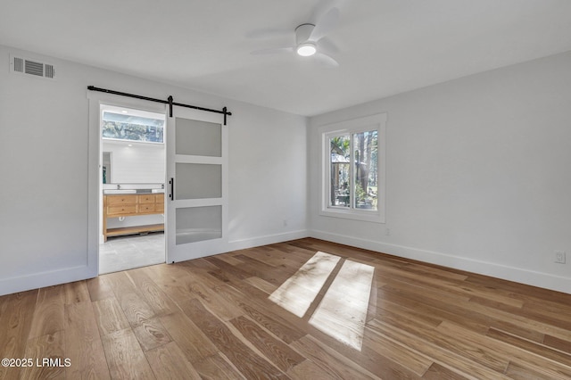 unfurnished bedroom with visible vents, baseboards, a barn door, wood finished floors, and ensuite bath