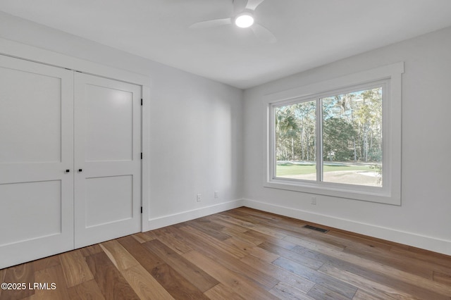 unfurnished room with ceiling fan, wood finished floors, visible vents, and baseboards