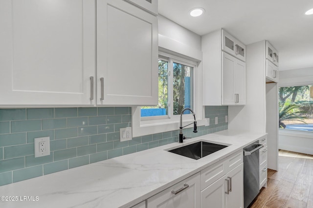 kitchen with light stone counters, backsplash, white cabinetry, and a sink