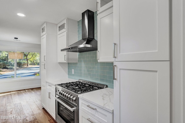 kitchen featuring backsplash, wood finished floors, high end range, white cabinets, and wall chimney exhaust hood