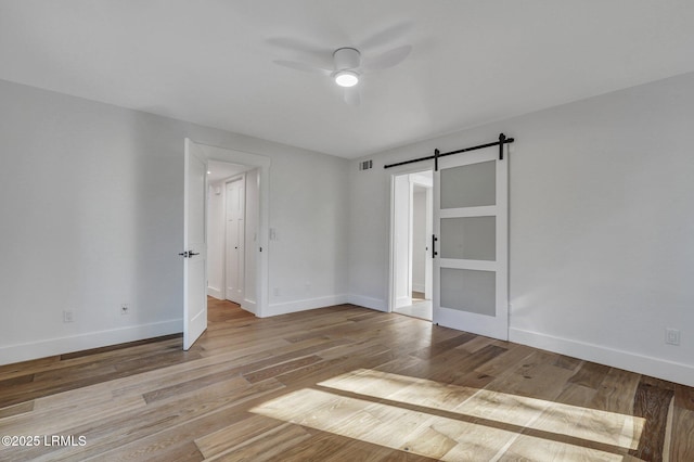 unfurnished room featuring visible vents, a ceiling fan, wood finished floors, a barn door, and baseboards