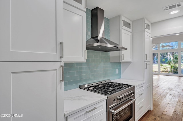 kitchen with visible vents, stainless steel gas stove, backsplash, wall chimney exhaust hood, and white cabinets