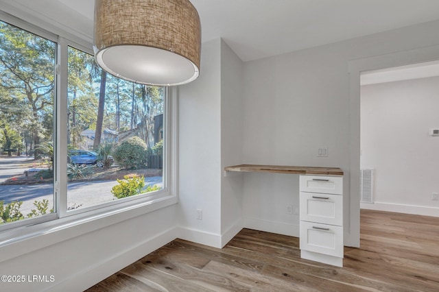 unfurnished dining area with wood finished floors, visible vents, and baseboards