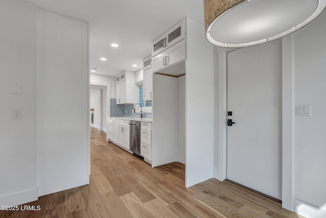 kitchen featuring backsplash, light wood finished floors, glass insert cabinets, dishwasher, and light countertops