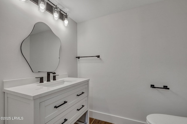 half bathroom with vanity, toilet, wood finished floors, and baseboards