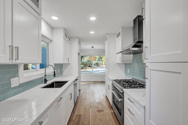 kitchen with a sink, stainless steel appliances, wall chimney exhaust hood, and white cabinetry