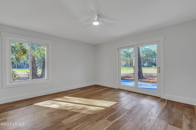 spare room featuring plenty of natural light, baseboards, wood-type flooring, and ceiling fan