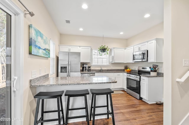 kitchen with visible vents, stone countertops, white cabinetry, stainless steel appliances, and a peninsula