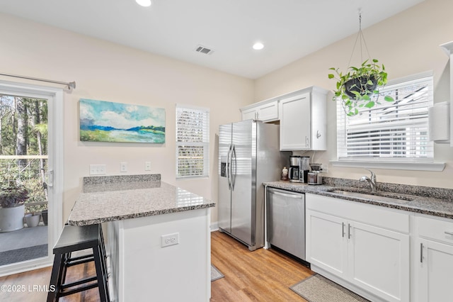 kitchen featuring visible vents, a kitchen bar, a sink, white cabinetry, and appliances with stainless steel finishes