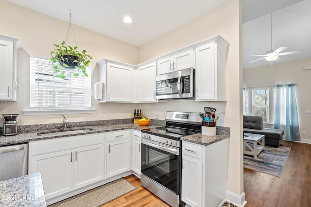 kitchen with a sink, dark stone countertops, light wood-style floors, appliances with stainless steel finishes, and white cabinets