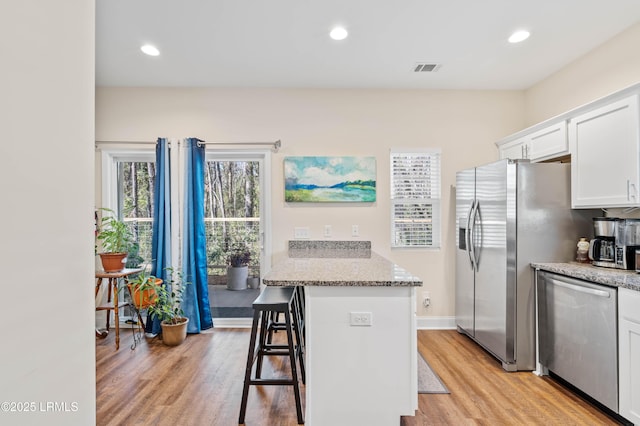 kitchen featuring light wood-type flooring, recessed lighting, stainless steel appliances, a breakfast bar area, and white cabinets