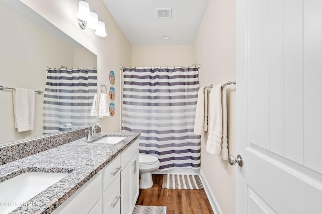 full bath featuring wood finished floors, visible vents, double vanity, a sink, and toilet