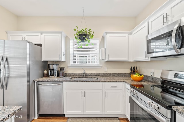 kitchen with stone counters, white cabinets, stainless steel appliances, and a sink