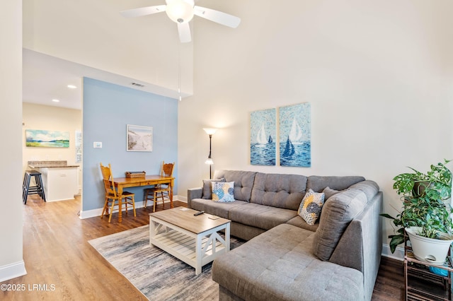 living room featuring visible vents, wood finished floors, a towering ceiling, baseboards, and ceiling fan