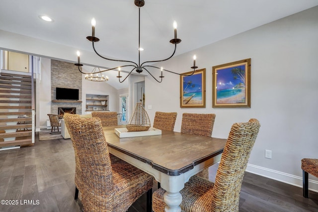 dining room featuring lofted ceiling, dark wood-style floors, a fireplace, baseboards, and a chandelier