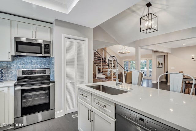 kitchen with backsplash, light countertops, appliances with stainless steel finishes, an inviting chandelier, and a sink