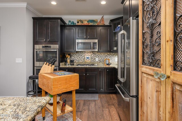 kitchen with appliances with stainless steel finishes, dark hardwood / wood-style floors, backsplash, ornamental molding, and light stone countertops