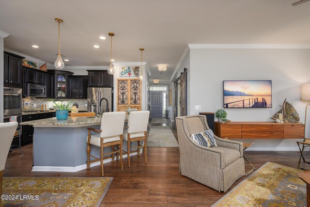 kitchen featuring appliances with stainless steel finishes, backsplash, a center island with sink, dark hardwood / wood-style flooring, and a barn door