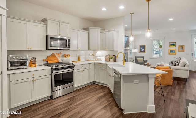 kitchen with dark wood-type flooring, stainless steel appliances, a kitchen bar, decorative light fixtures, and kitchen peninsula