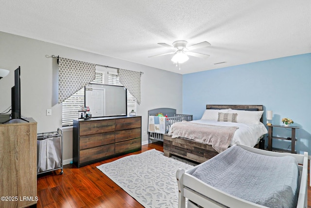 bedroom featuring dark wood finished floors, visible vents, a ceiling fan, a textured ceiling, and baseboards