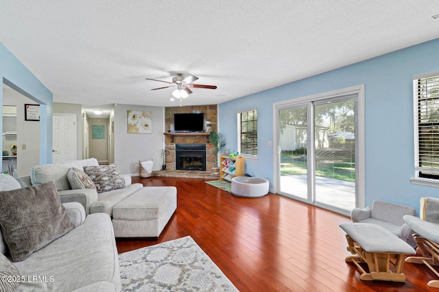 living room with a textured ceiling, a stone fireplace, wood-type flooring, and a ceiling fan