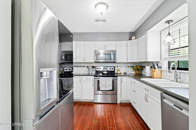 kitchen with stainless steel appliances, dark wood-style flooring, a sink, and white cabinets