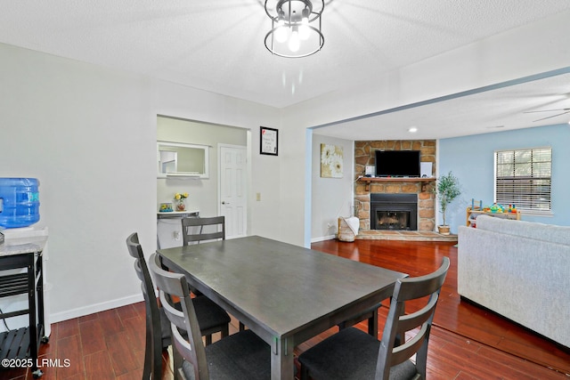 dining space with a textured ceiling, a fireplace, baseboards, and wood finished floors