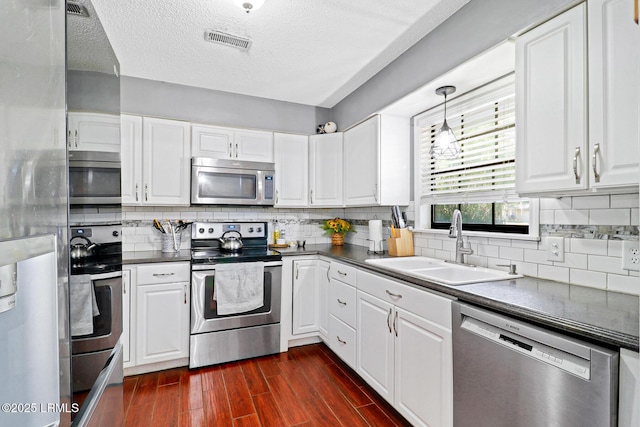 kitchen featuring dark wood finished floors, stainless steel appliances, dark countertops, visible vents, and a sink