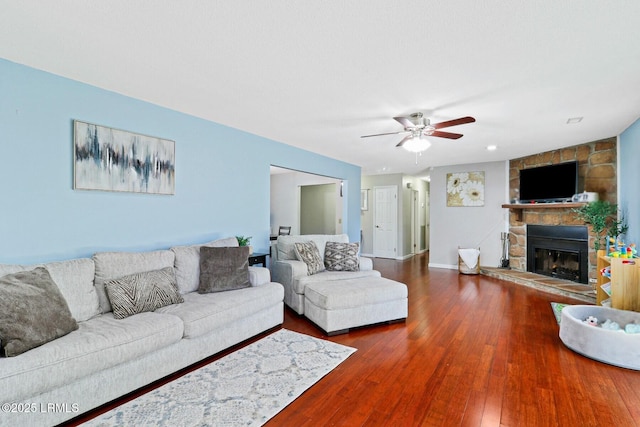 living room with ceiling fan, a stone fireplace, wood-type flooring, and baseboards