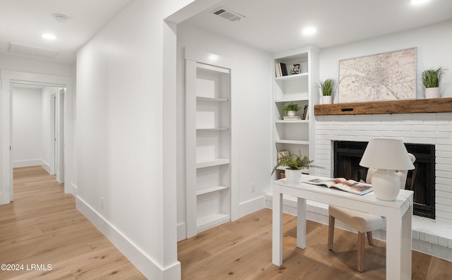 office featuring light wood-type flooring, a fireplace, and built in shelves