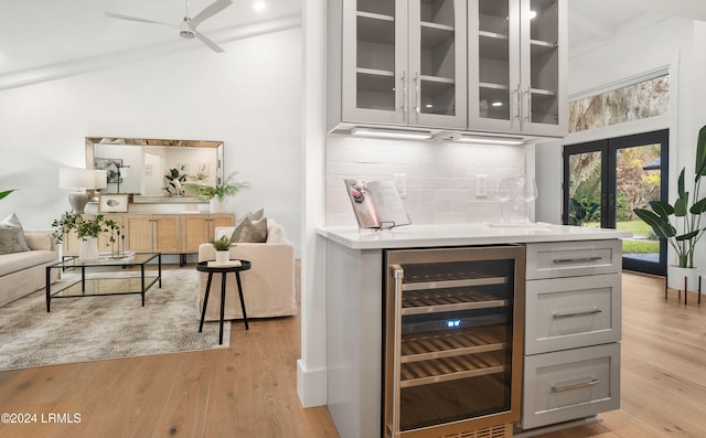 bar featuring french doors, gray cabinetry, light hardwood / wood-style flooring, beverage cooler, and decorative backsplash