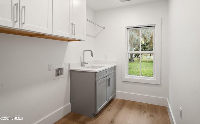 clothes washing area with cabinets, sink, washer hookup, and light hardwood / wood-style floors