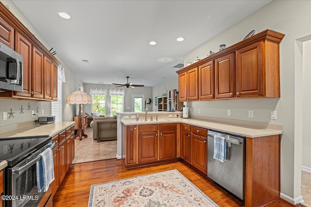 kitchen featuring sink, ceiling fan, appliances with stainless steel finishes, kitchen peninsula, and light wood-type flooring