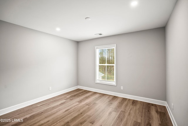 empty room featuring wood finished floors, visible vents, and baseboards