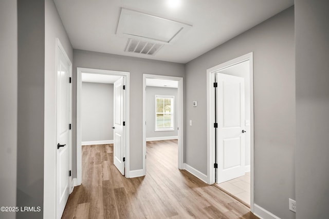 corridor with light wood-style floors, attic access, visible vents, and baseboards