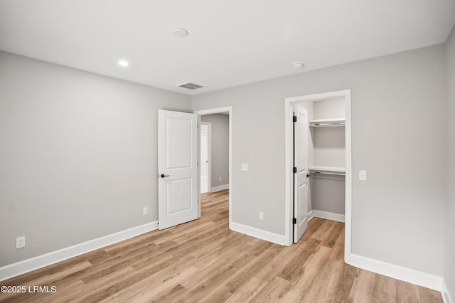 unfurnished bedroom with a walk in closet, visible vents, light wood finished floors, and baseboards