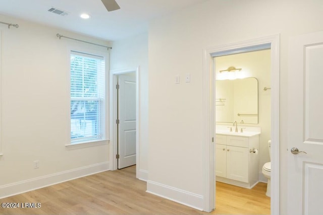 unfurnished bedroom featuring ceiling fan, ensuite bathroom, sink, and light hardwood / wood-style floors