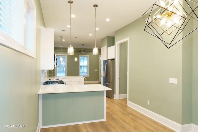 kitchen with white cabinetry, decorative light fixtures, light hardwood / wood-style flooring, stainless steel refrigerator, and kitchen peninsula