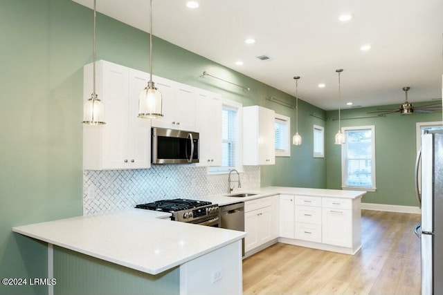 kitchen with sink, white cabinetry, appliances with stainless steel finishes, kitchen peninsula, and pendant lighting