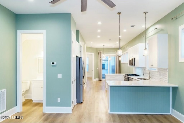 kitchen with sink, kitchen peninsula, pendant lighting, stainless steel appliances, and white cabinets